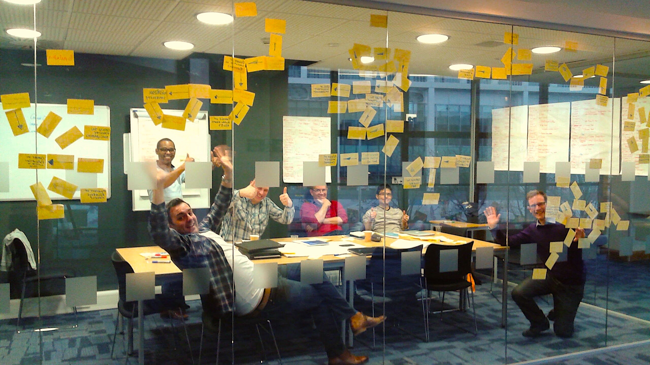 people in a glass walled room with post-it notes along the walls in a scenario planning session